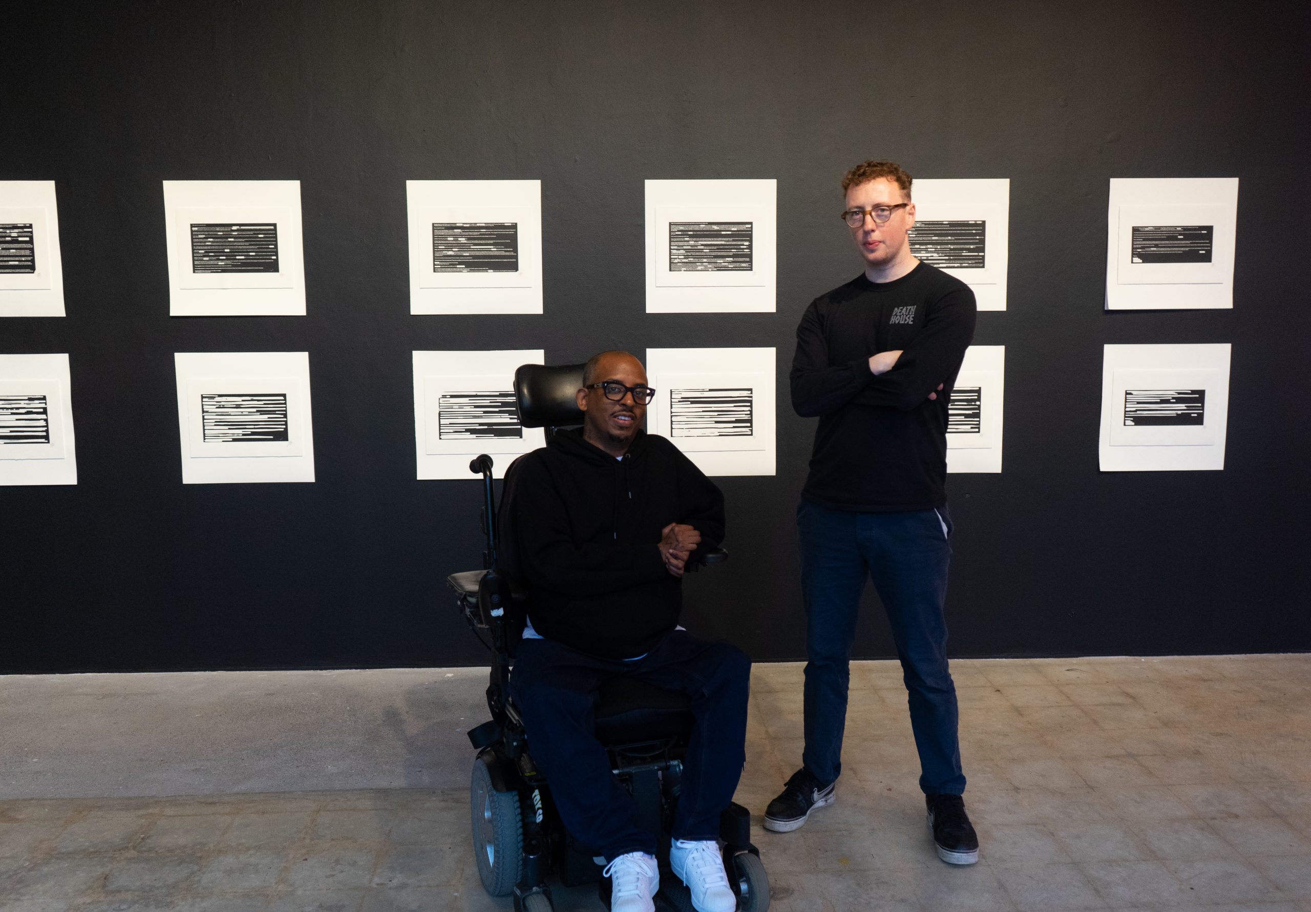 a man standing next to an artist in a wheelchair at his exhibition