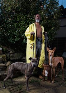 a man in a yellow long coat and no shirt, with chain mail trousers holding 3 dogs' leads