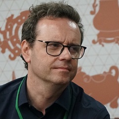 A man with short brown hair and glasses is looking at something off-camera.