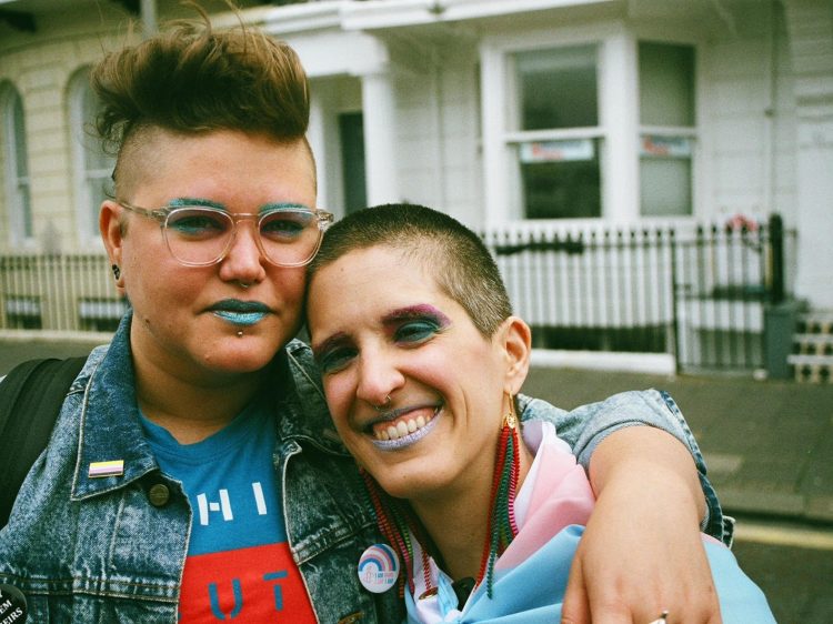 A couple hugging, wearing bright blue/green shiny makeup