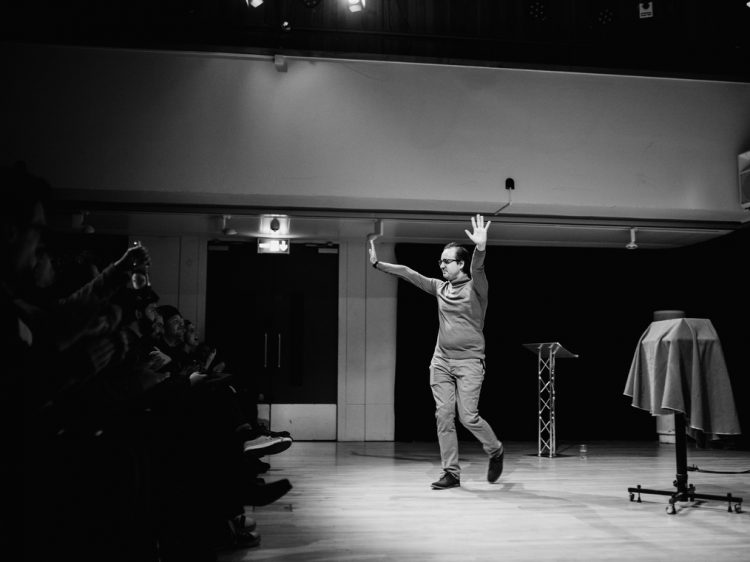 A man in a polo neck waves to a crowd at a symposium