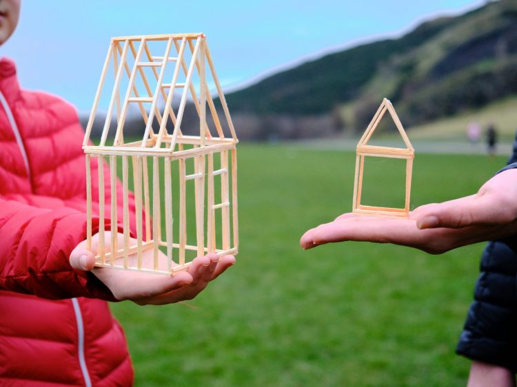 two people, a boy and man, hold models of houses on their palms