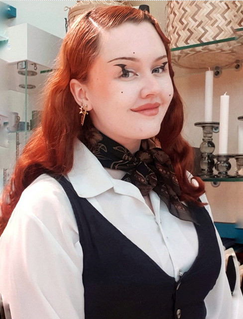A woman with red hair wearing a white shirt, cravat, and black waistcoat