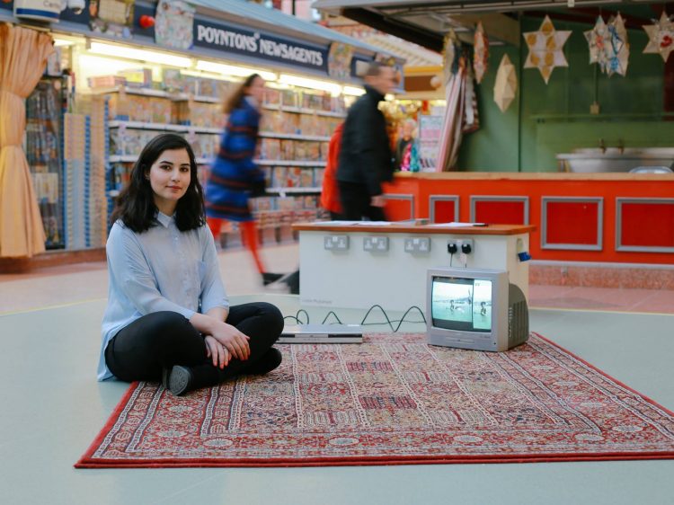 A woman sat on a rug in a busy market, with a crt tv