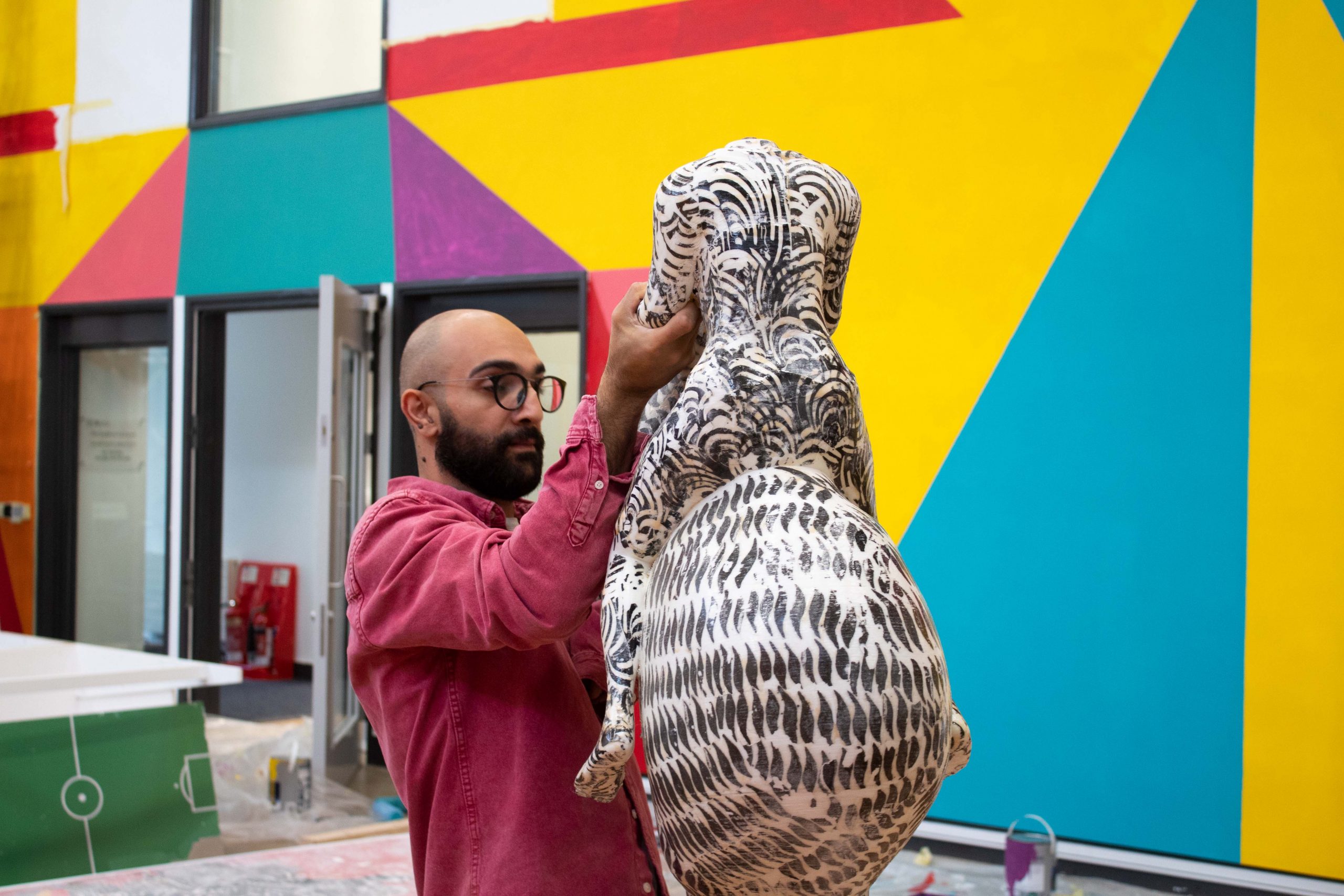Mohammad Barrangi holding up a black and white sculpture, with bright coloured walls behind him.