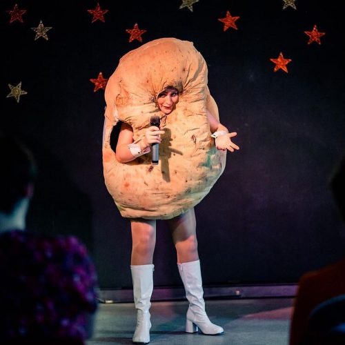 A women dressed as a potato with go-go boots, holding a microphone on stage.