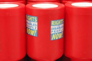 A close up of three red charity tins, with two stickers on the middle tin saying 'RIGHTS FOR DISABLED PEOPLE NOW!'.