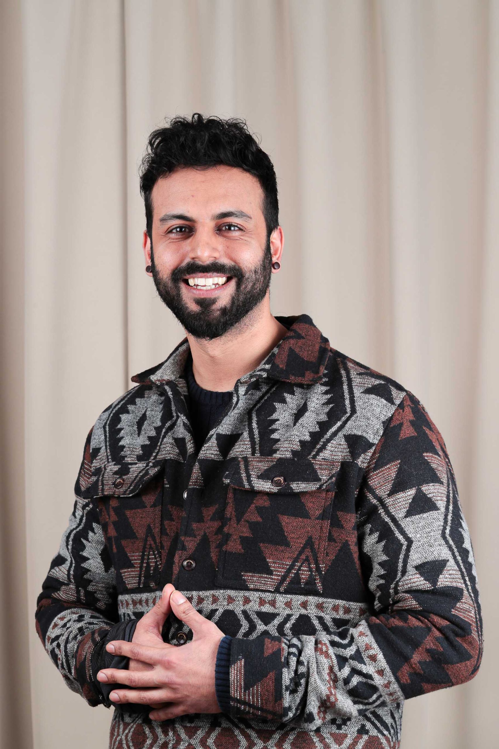 An Asian man with short black hair and a beard, smiling into the camera. He has his hands crossed in front of himself.