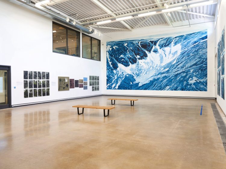 An open exhibition space with images on the walls and a large painting of the sea on the far wall.