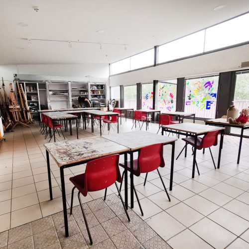 A large, bright room with art supplies on the walls. In the middle are tables and chairs set up like a classroom.