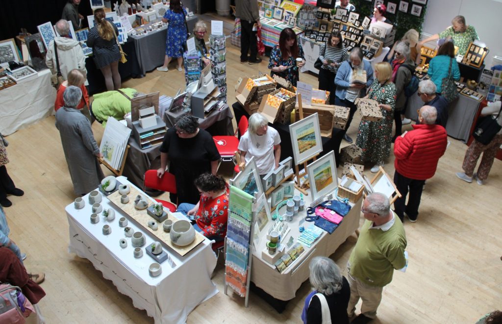 A top-down view of the main hall filled with people looking at various stands full of handmade arts and crafts.