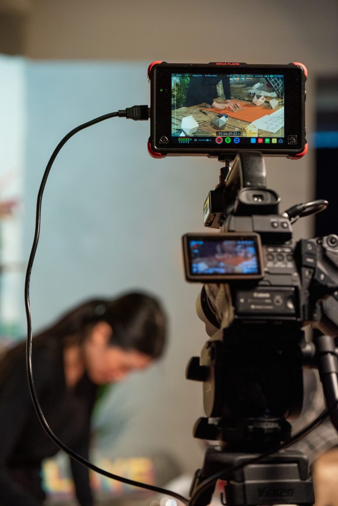 A high-tech camera recording a person in the background creating with paper and her hands.