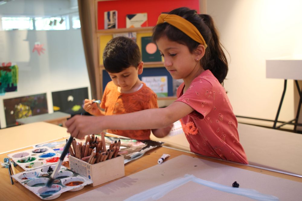 Two children using paint brushes to pick up paints.