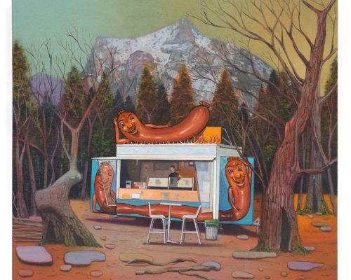 A hotdog stand sits in the middle of a woodland clearing with a mountain in the background.