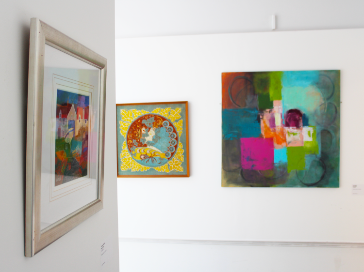Three framed, colourful works of art hanging on white walls.