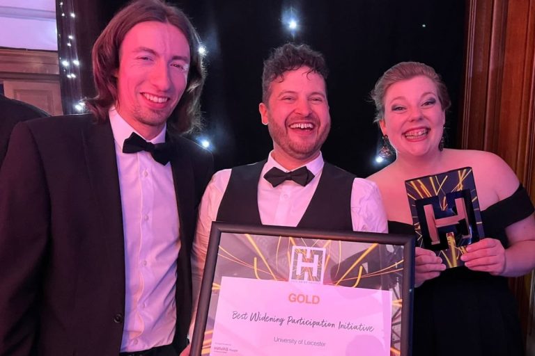 Two white men and a white women dressed in formal attire holding up a framed certificate and smiling.