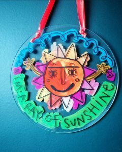 Handpainted round piece of perspex glass of a sun with text along the edge that reads 'I'm a ray of sunshine'