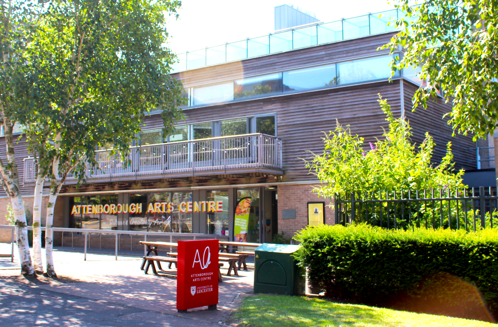 The outside of Attenborough Arts Centre building on a sunny day. On the windows is painted the name of the centre.