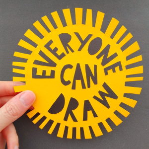 A round piece of paper cut out resembling the sun with 'Everyone Can Draw' cut out in the centre.
