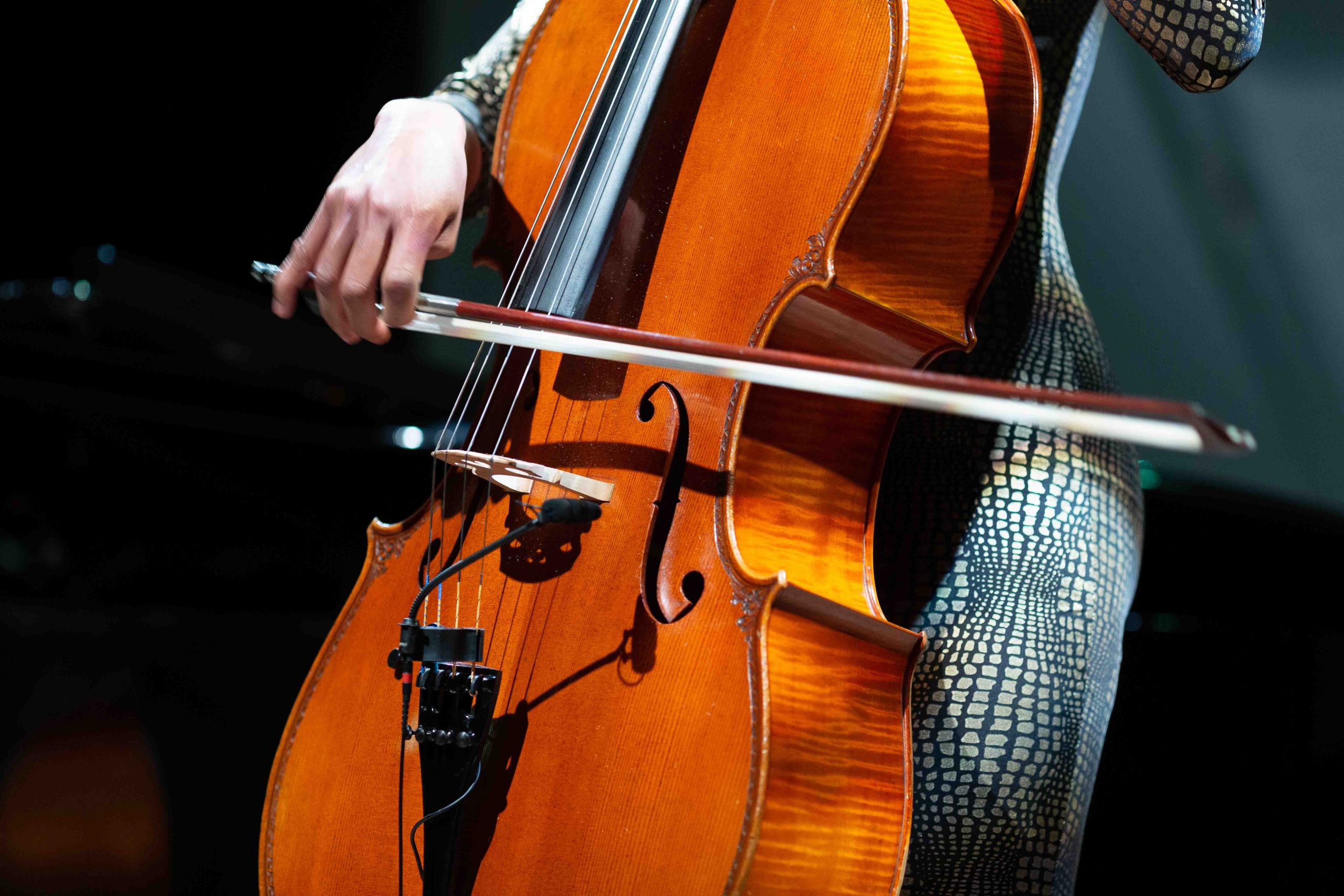 A close up of a hand playing a cello in the dark.