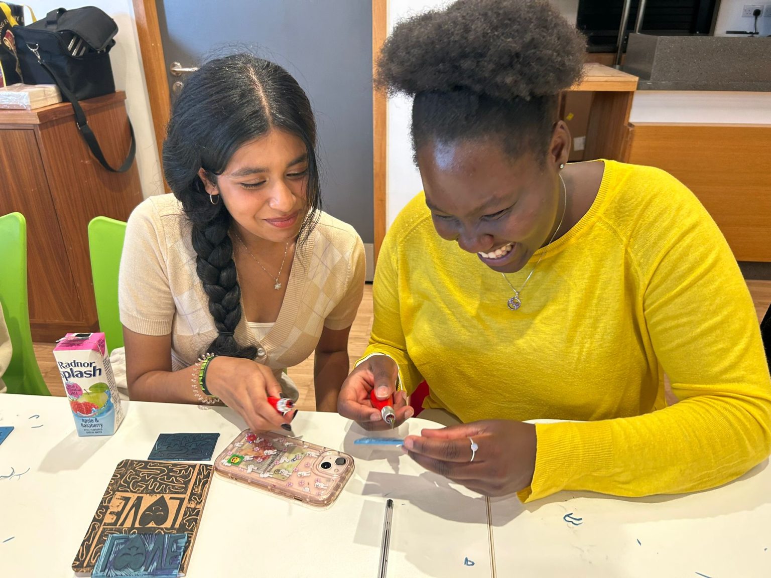 Two women working on a lino print together while smiling.