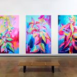 Three huge and colourful botanical paintings on a white gallery wall with a bench in front of it.