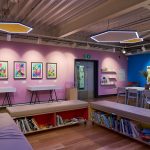 A colourful room with pink and blue walls, hanging artwork on them. In the middle of the room are tables and chairs.