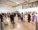 A large group of people wander around a large, white gallery space looking at the artwork.