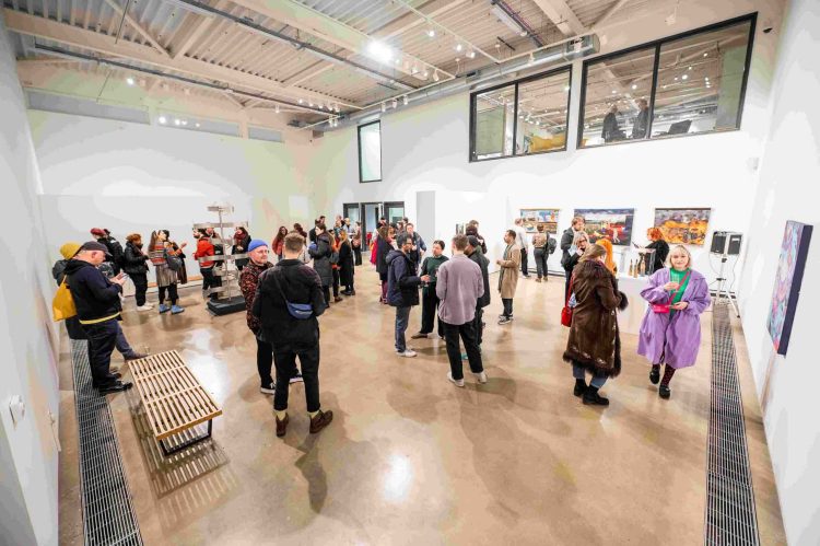 A large group of people wander around a large, white gallery space looking at the artwork.