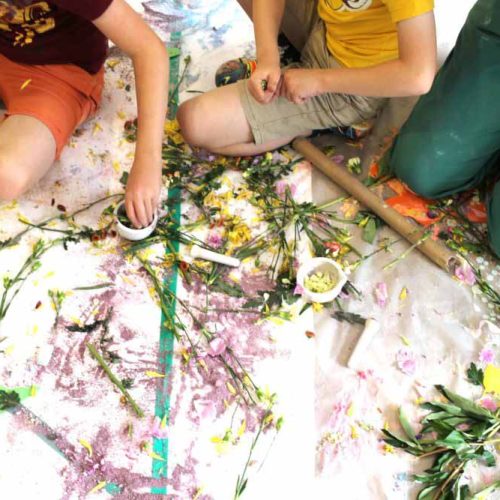 Three children sat on the floor making marks on a paint covered floor.