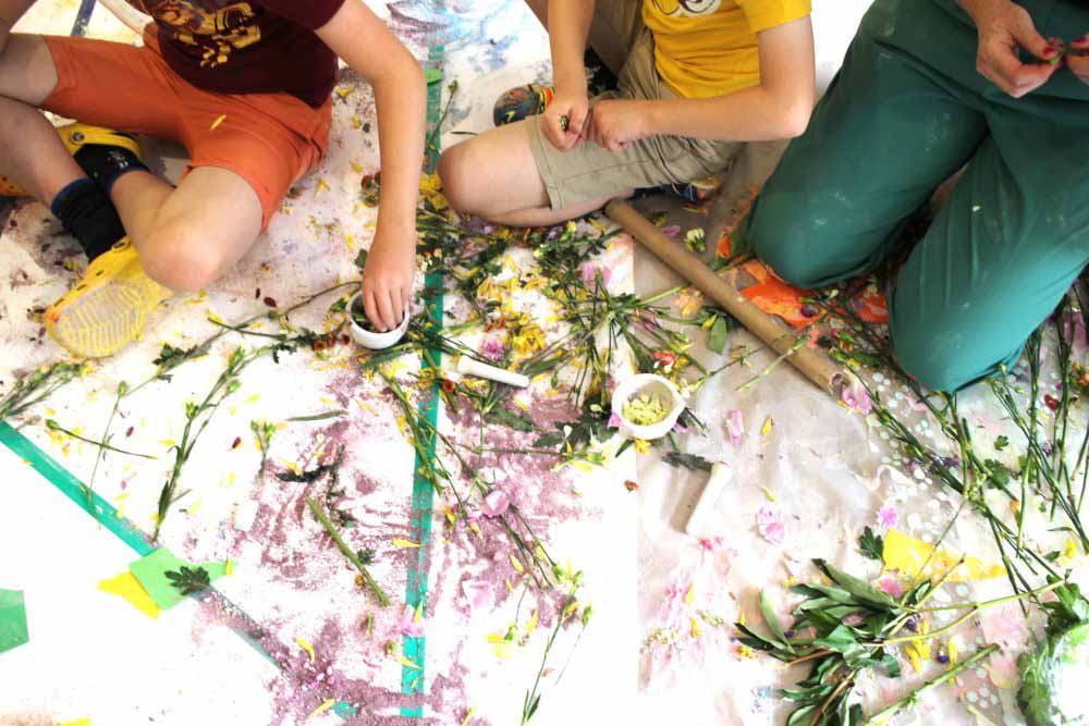 Three children sat on the floor making marks on a paint covered floor.