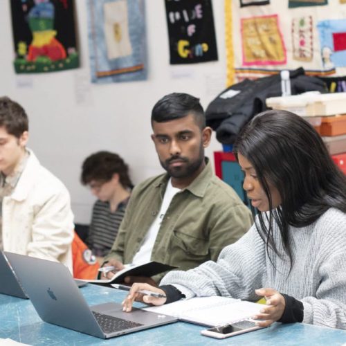 Three young people sat at a desk with laptops working together.