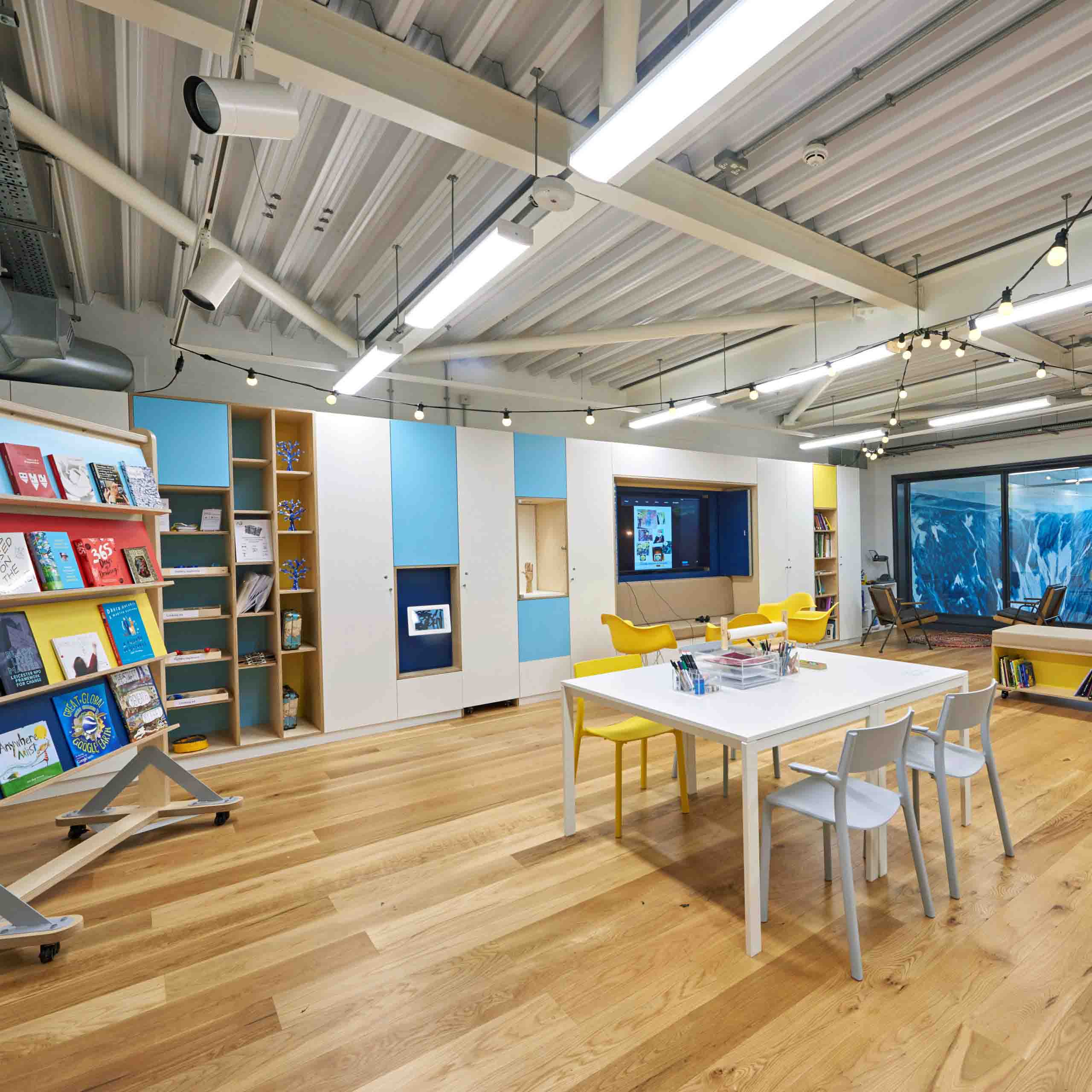 A community room with blue and white cupboards, books on shelves, a large tv and table and chairs in the middle.