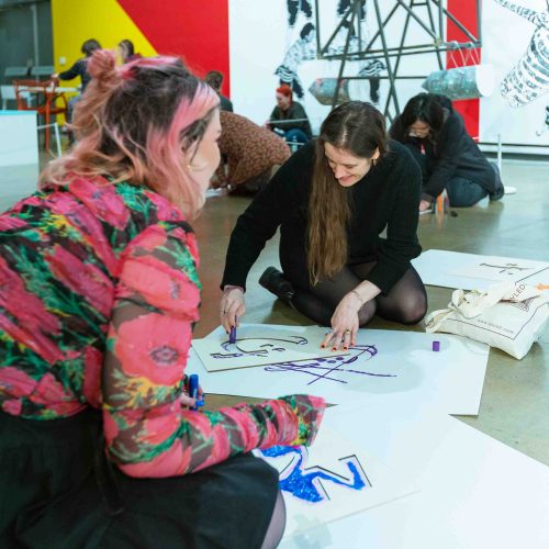 A group of young people sitting on the floor of an art gallery drawing on large pieces of paper.