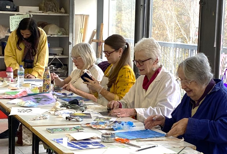 A group of women sat around a table filled with paints and paper, creating art.