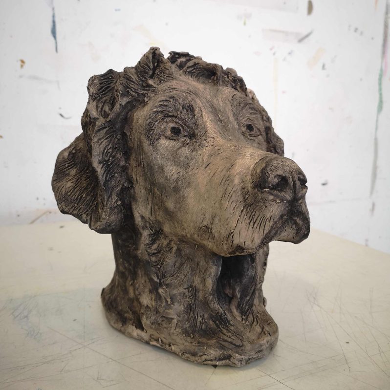 A realistic dogs head carved out of grey clay.