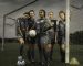 A group of women footballers stood in a pitch with the goal, on a dark and stormy day.