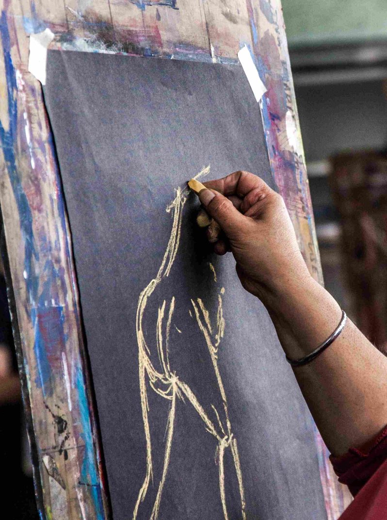 A hand drawing a figure onto black paper with white chalk.