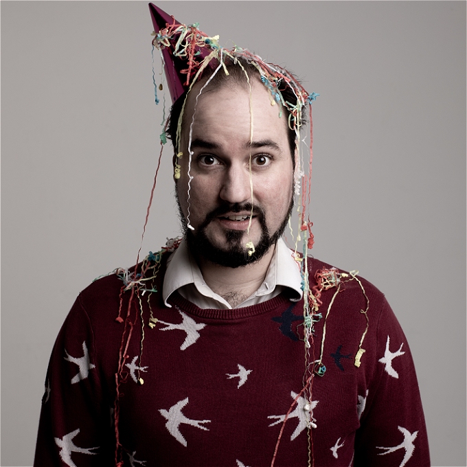 A white bearded man covered in confetti wearing a party hat.