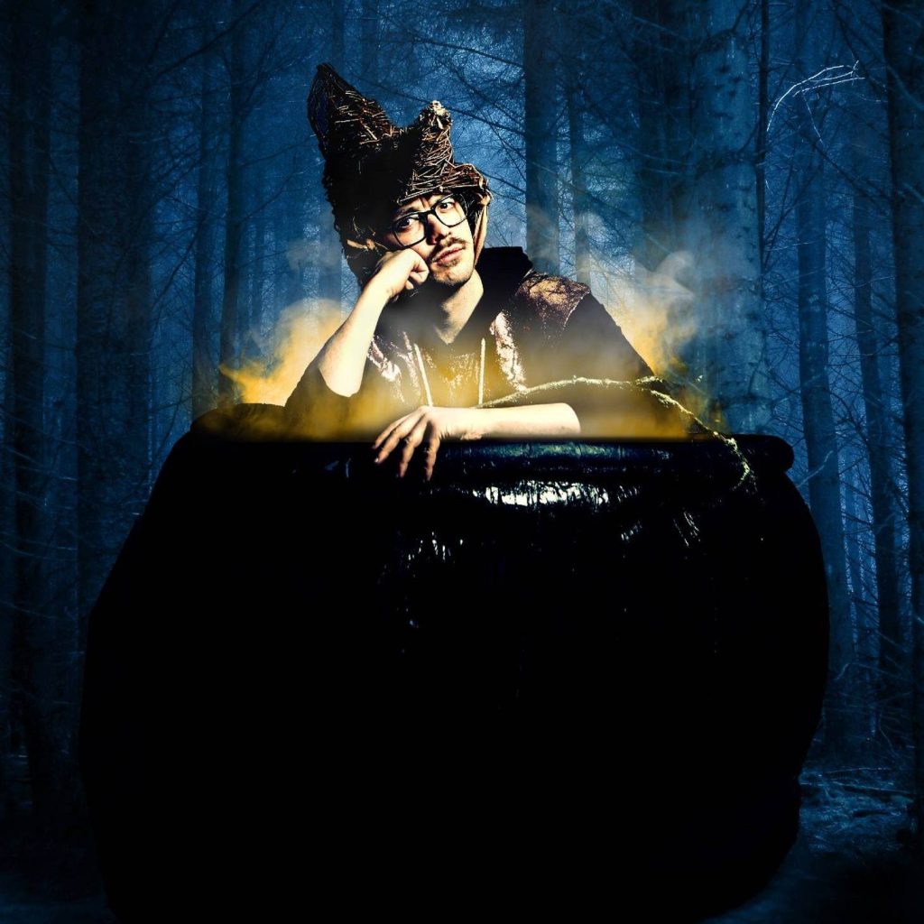 A man resting his head on his hand in a cauldron in the middle of the woods.