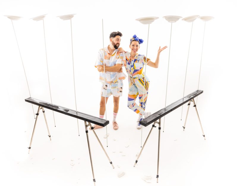 A man and a women in a white room with spinning paper plates around them.