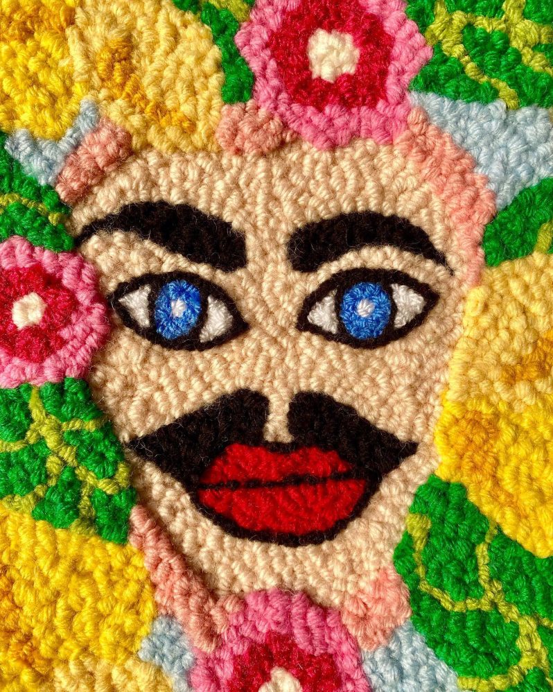 A punch needle of a moustached face surrounded by flowers.