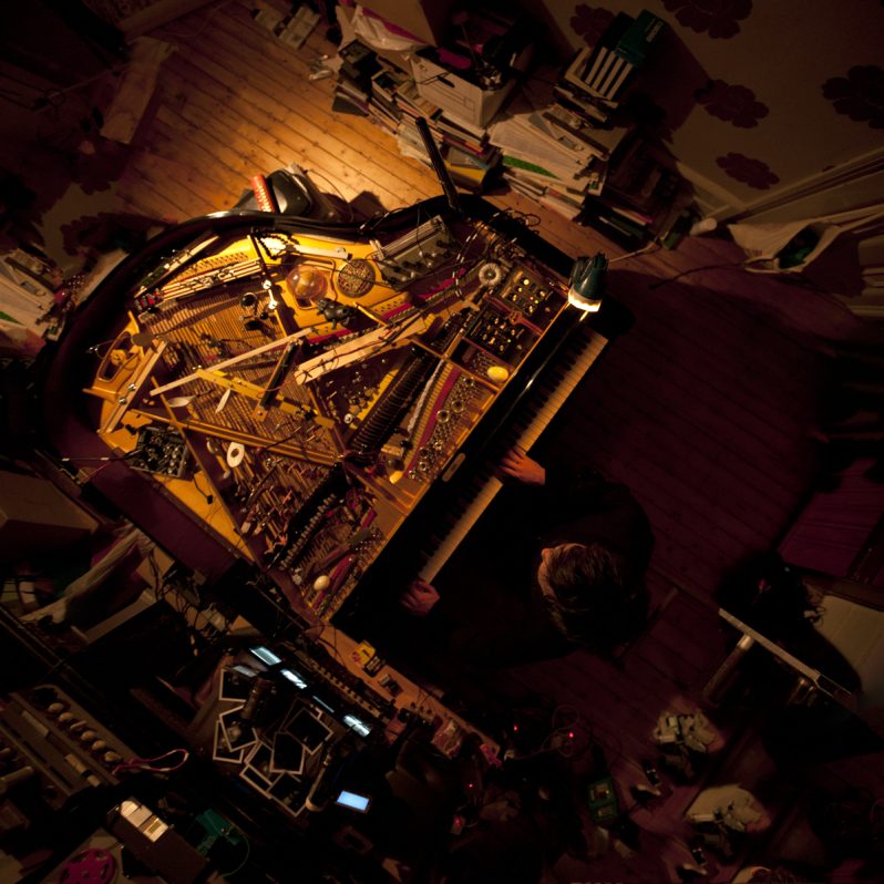 A over-the-top shot of a piano with its case open showing all the inner strings as someone plays it in a dark and cluttered room.