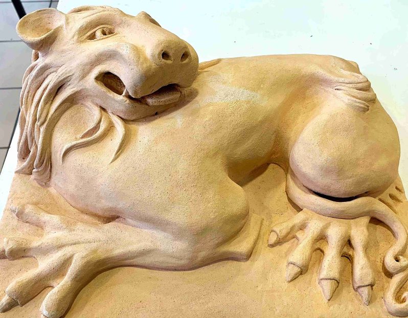 A stylistic clay lion laying down.