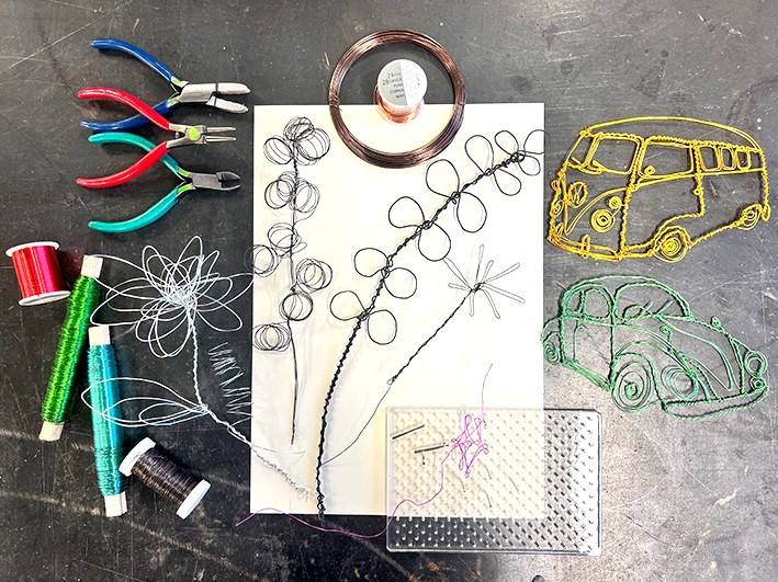 Pieces of wire twirled into different shapes such as flowers and cars laid on a work desk.