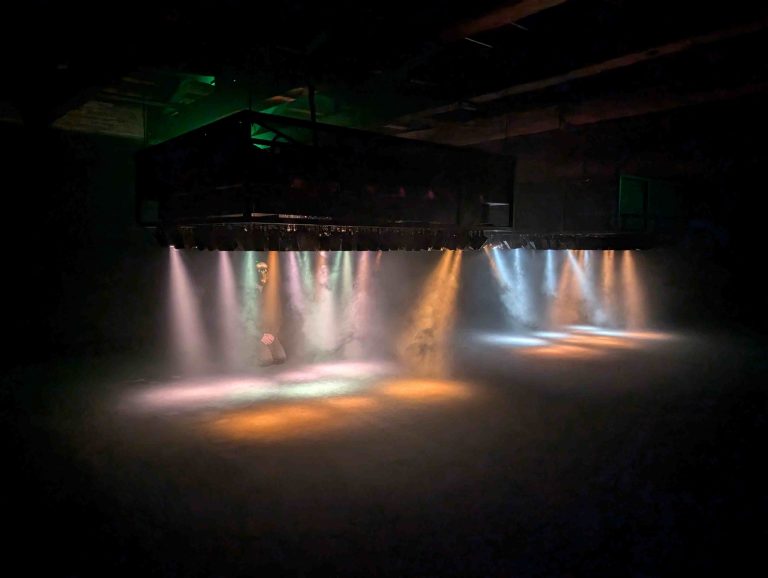 A dark room with low lights putting out pastel coloured light beams onto the floor with smoke everywhere.