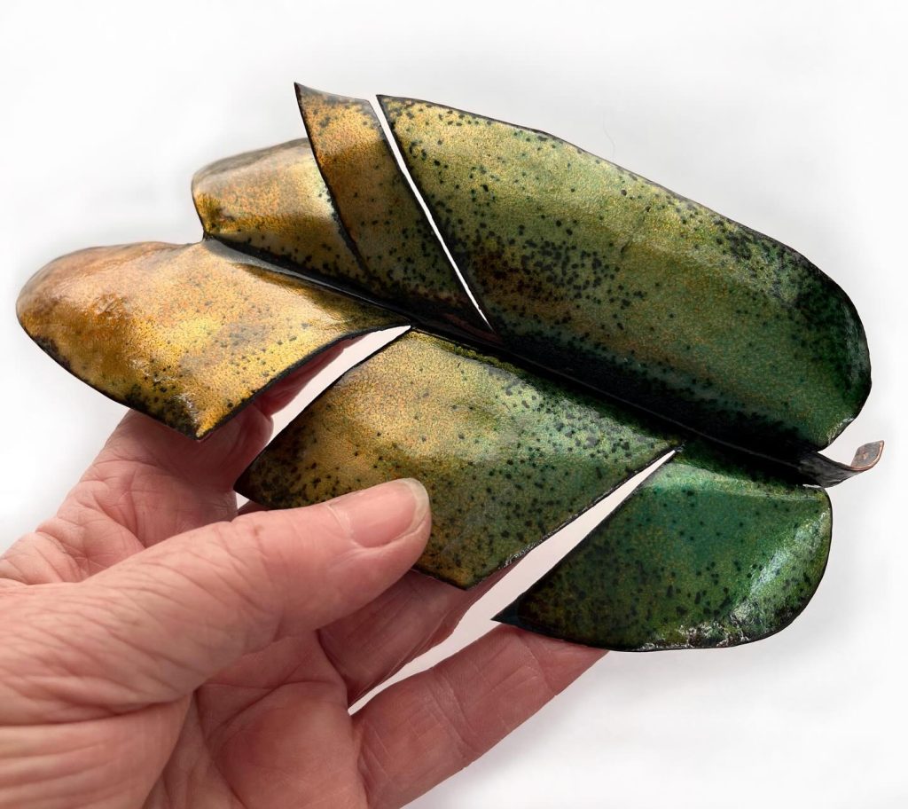 A green and gold leaf made of metal held up by a hand.