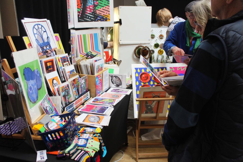 A range of colourful cards and posters displayed on a table, with people looking over them.