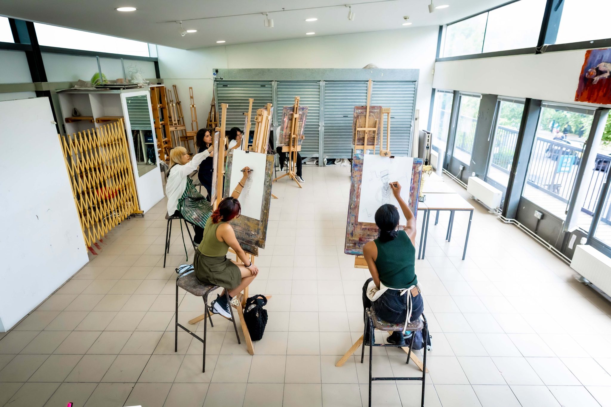 A group of people in a circle with easels drawing on paper, in an art studio.