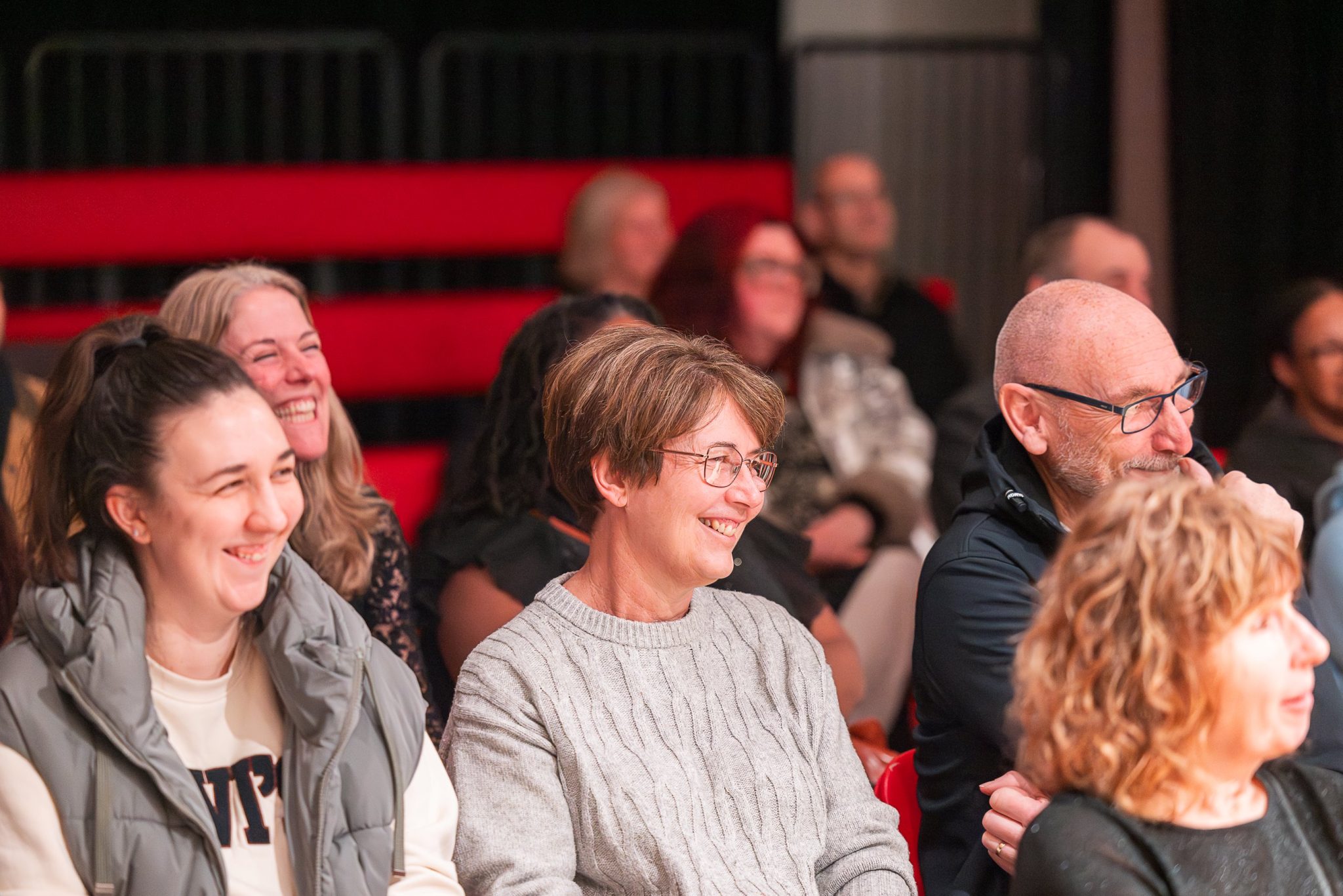 A group of people sat in an audiences, smiling and laughing.